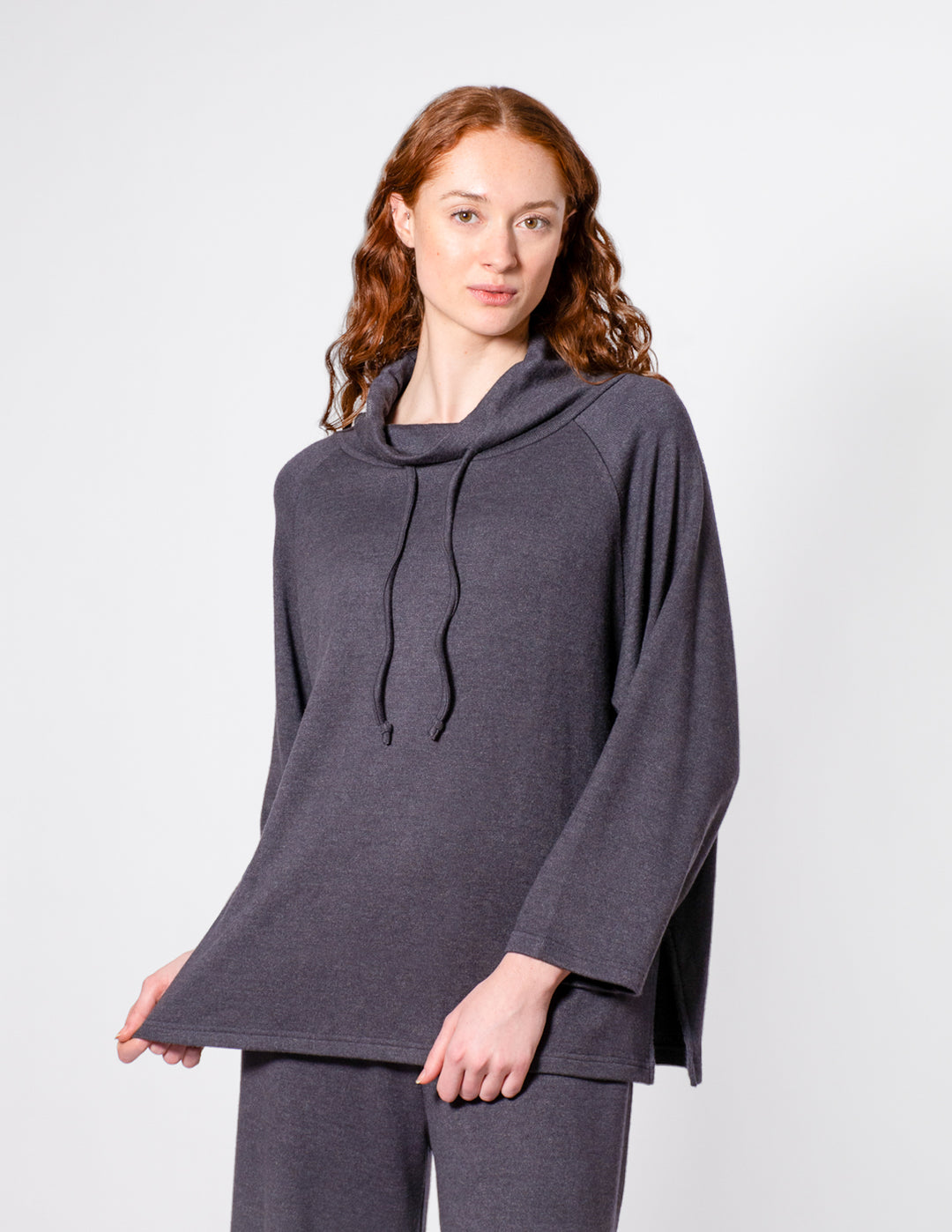 Woman wearing a dark gray long-sleeve top with a hood on a white background