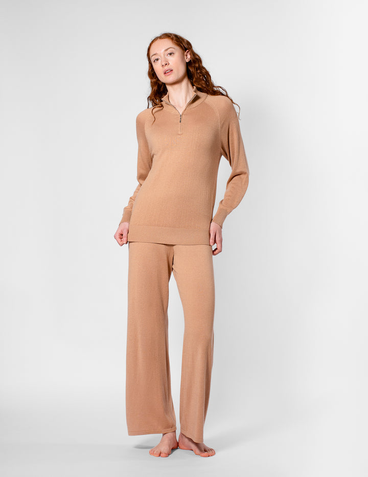 Woman wearing a beige long-sleeve top and wide-leg pants on a white background