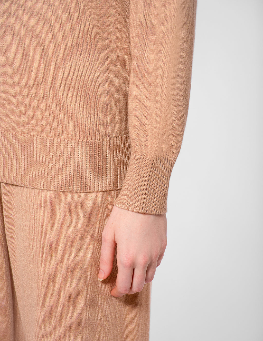 Close-up of a person wearing a beige sweater and pants on a white background