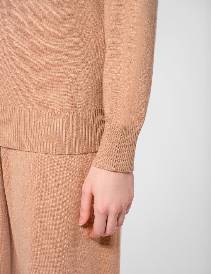Close-up of a person wearing a beige sweater and pants on a white background