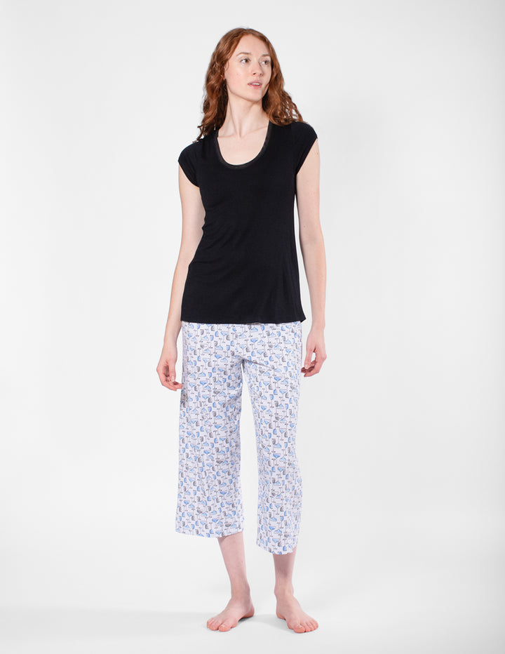 Woman wearing a black top and patterned capri pants on a white background