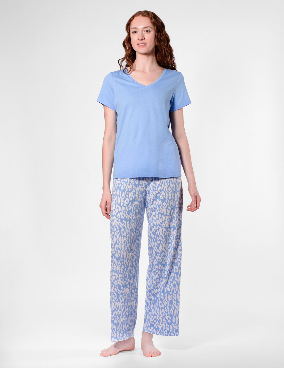 Woman wearing a light blue pajama top and patterned pants on a white background