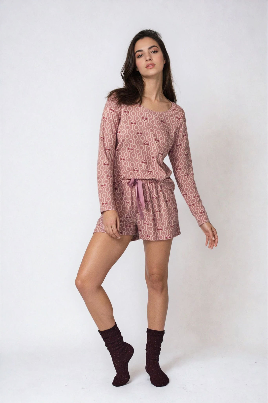 Woman wearing a pink floral pajama set with maroon socks on a white background