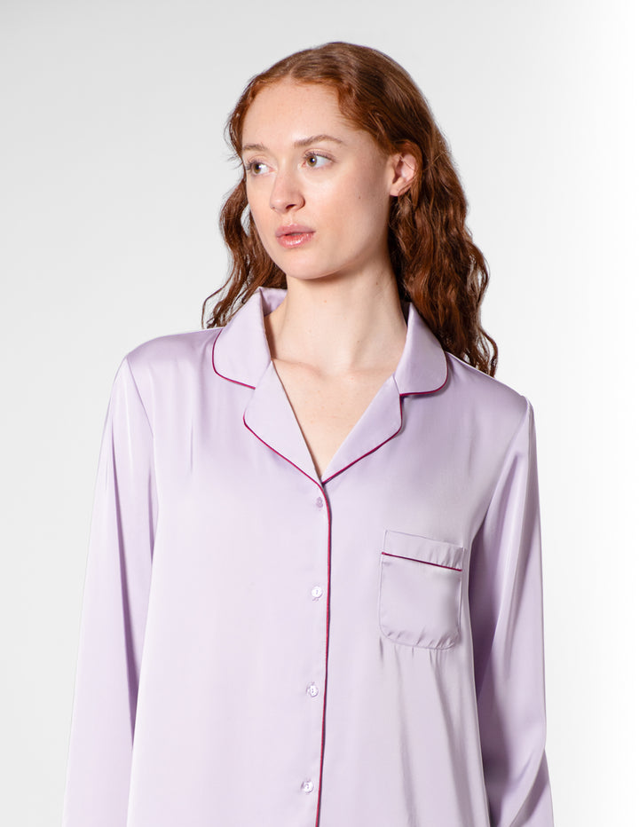 Woman wearing a light purple pajama top with pink piping on a white background