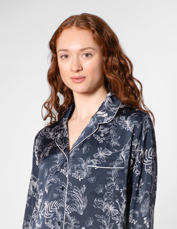 Woman wearing a navy blue pajama top with white floral pattern on a plain background