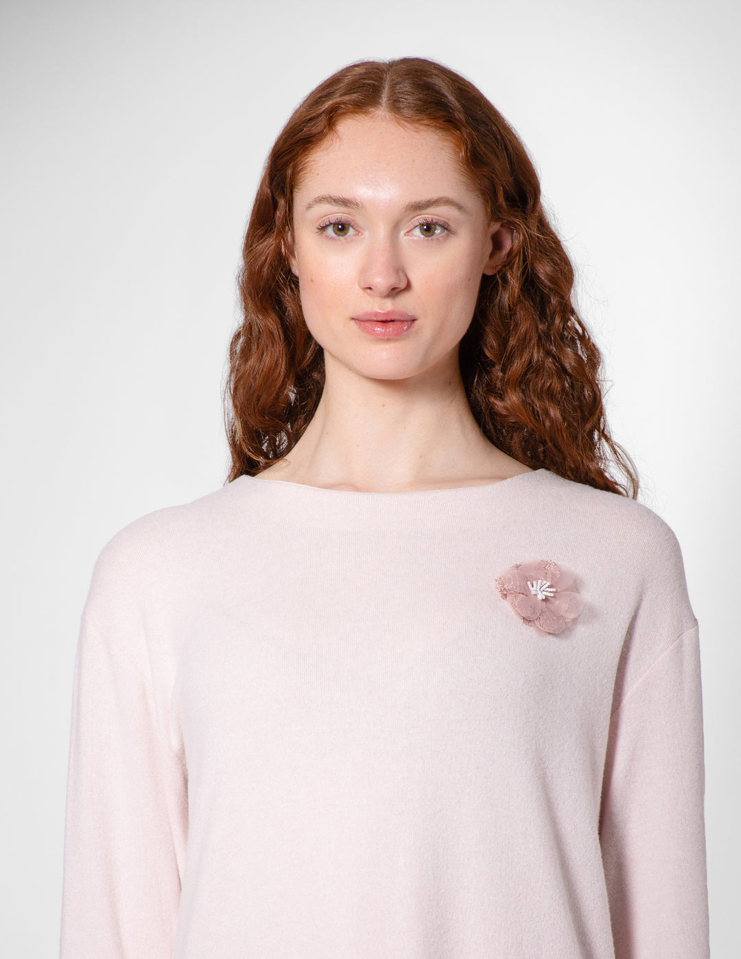 Woman wearing a light pink sweater with a floral design on a white background