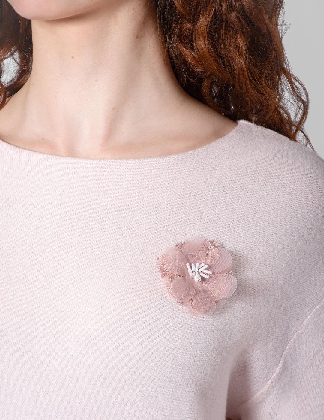 Pink floral brooch on a light pink sweater against a neutral background