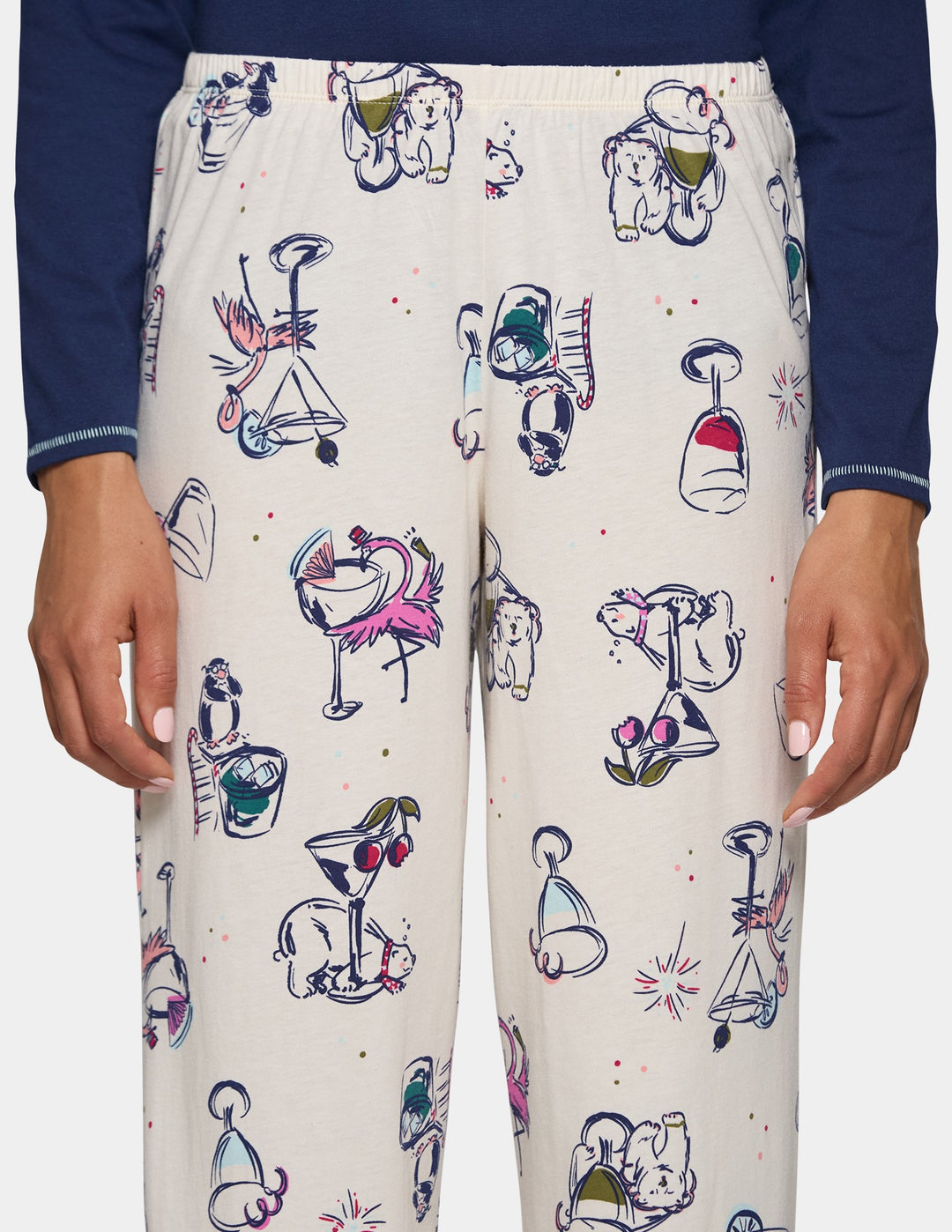 A closeup view of model wearing off-white pajama pants featuring an animal print design, pair with a long sleeve blue top.