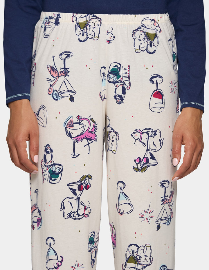 A closeup view of model wearing off-white pajama pants featuring an animal print design, pair with a long sleeve blue top.