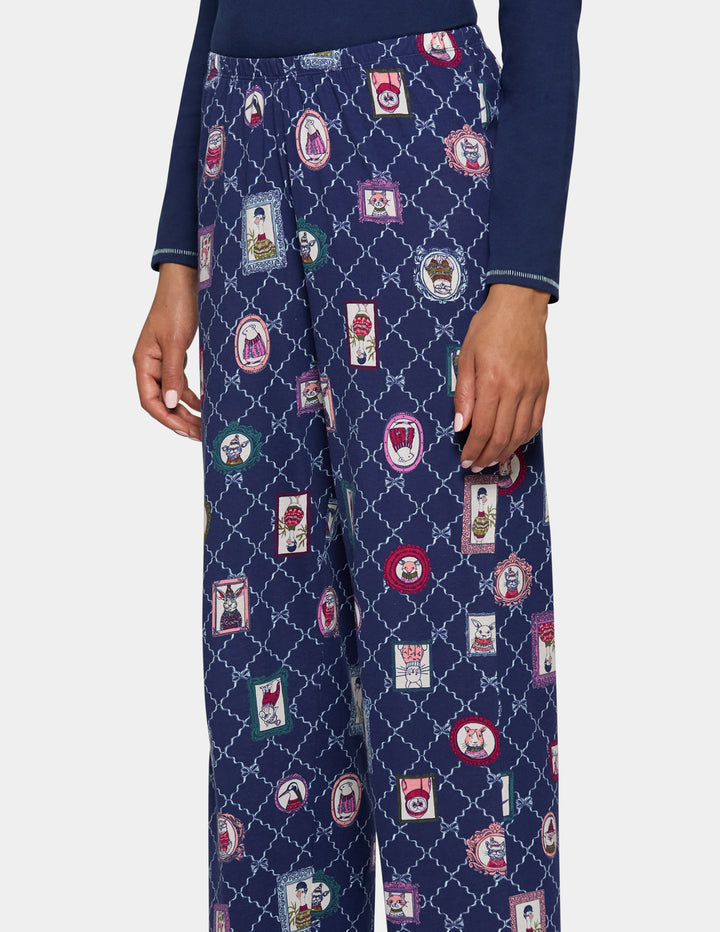 A person wearing navy blue wide-leg trousers with an allover embroidered patchwork and trellis pattern, paired with a navy long-sleeve top, shown against a light gray studio background.
