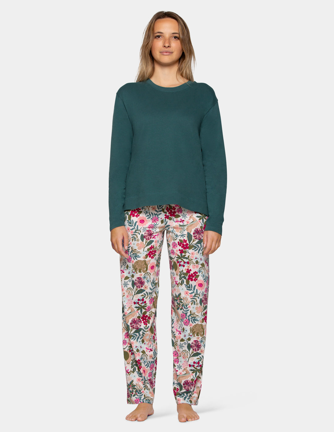 A woman modeling a two-piece pajama set consisting of a solid dark teal long-sleeve top and matching floral print pants with pink, red, and green flowers on a light gray background.