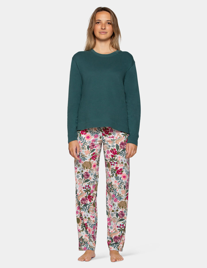 A woman modeling a two-piece pajama set consisting of a solid dark teal long-sleeve top and matching floral print pants with pink, red, and green flowers on a light gray background.