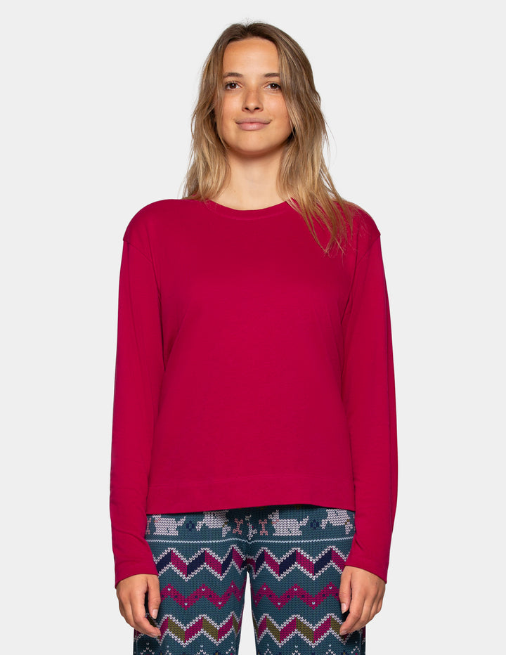 A woman modeling a bright magenta long-sleeve crewneck top against a light gray studio background, paired with patterned pj pants.