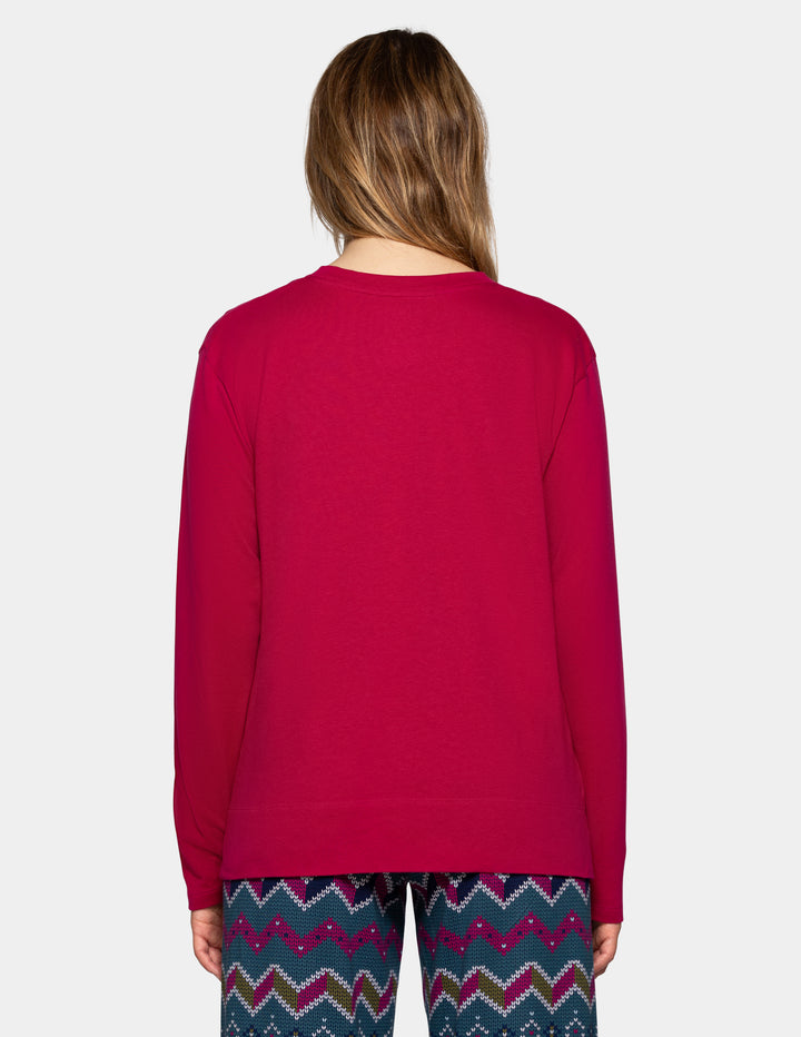 A woman viewed from the back wearing a solid magenta long-sleeve crewneck top and patterned pj pants with a colorful chevron design.