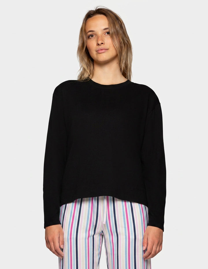 A woman wearing a black long-sleeve crewneck sweater and pink, white, and blue striped pants, standing against a light gray background.