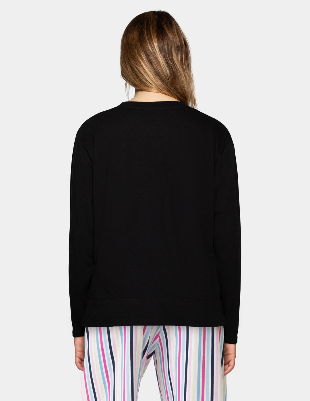 A woman viewed from the back wearing a plain black long-sleeve top and colorful vertically striped pants against a light gray studio background.