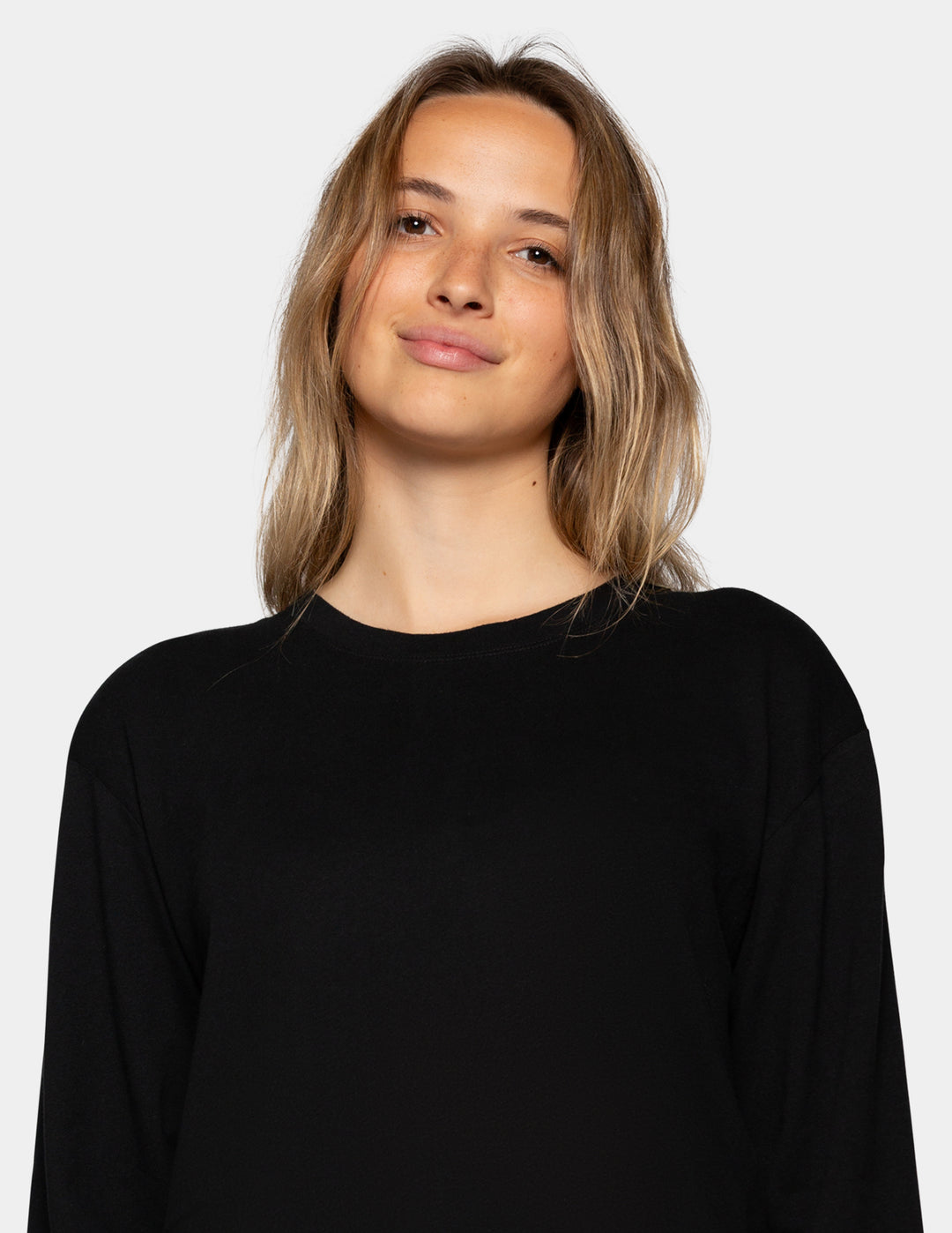 A woman with shoulder-length blonde hair wearing a black long-sleeve crewneck top, photographed against a solid light gray background.