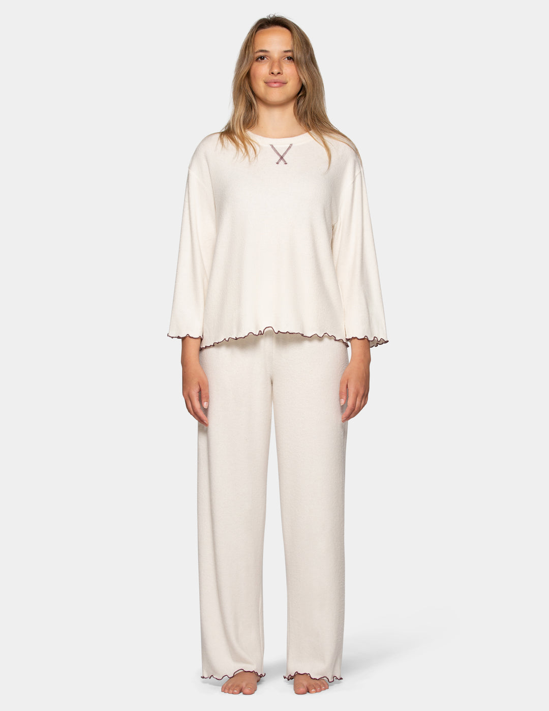 A model wearing an off-white pajama set featuring long pants and a long sleeve matching shirt.