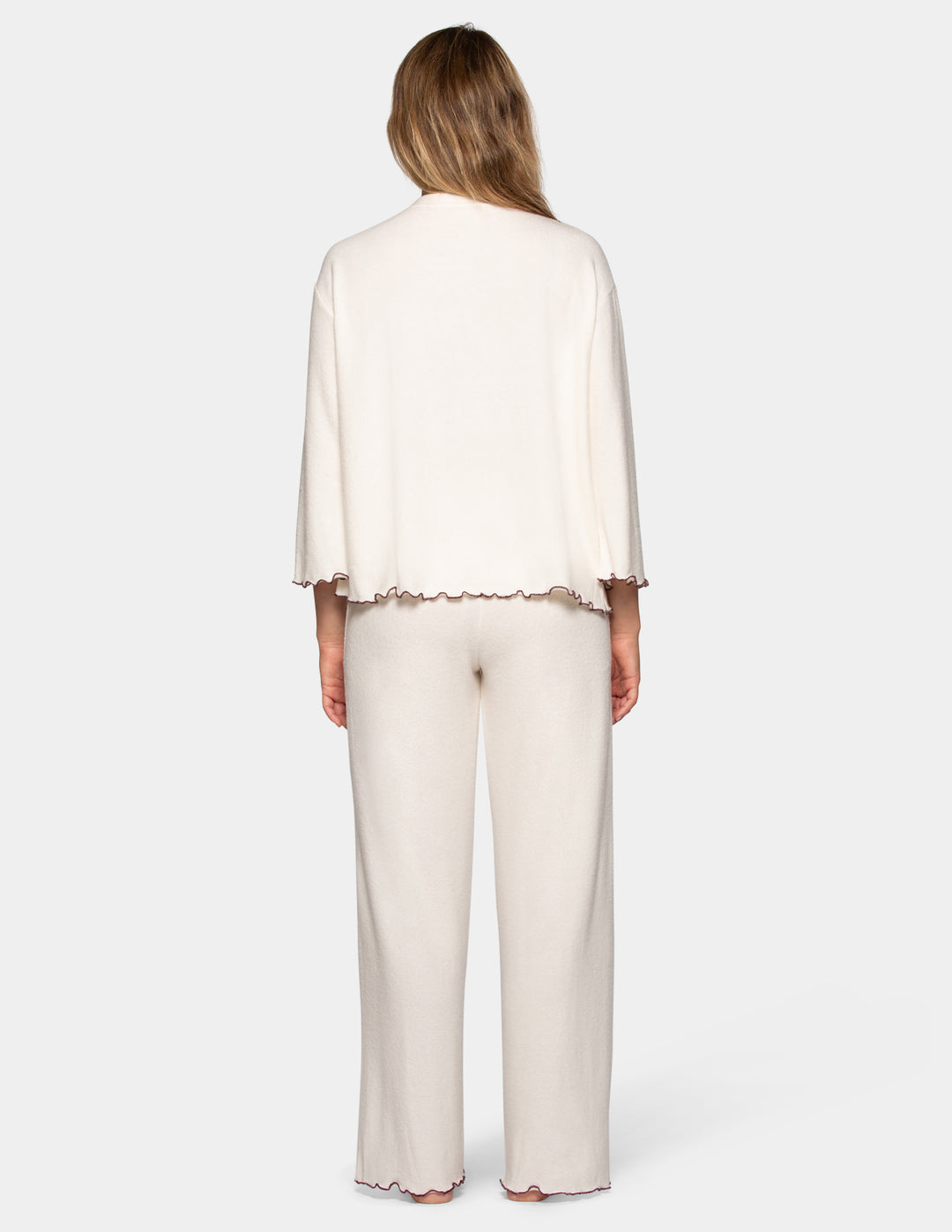 A back view of a model wearing an off-white pajama set featuring long pants and a long sleeve matching shirt.
