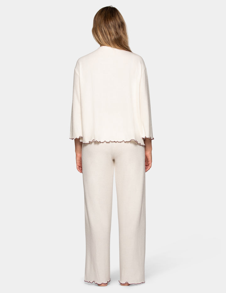 A back view of a model wearing an off-white pajama set featuring long pants and a long sleeve matching shirt.