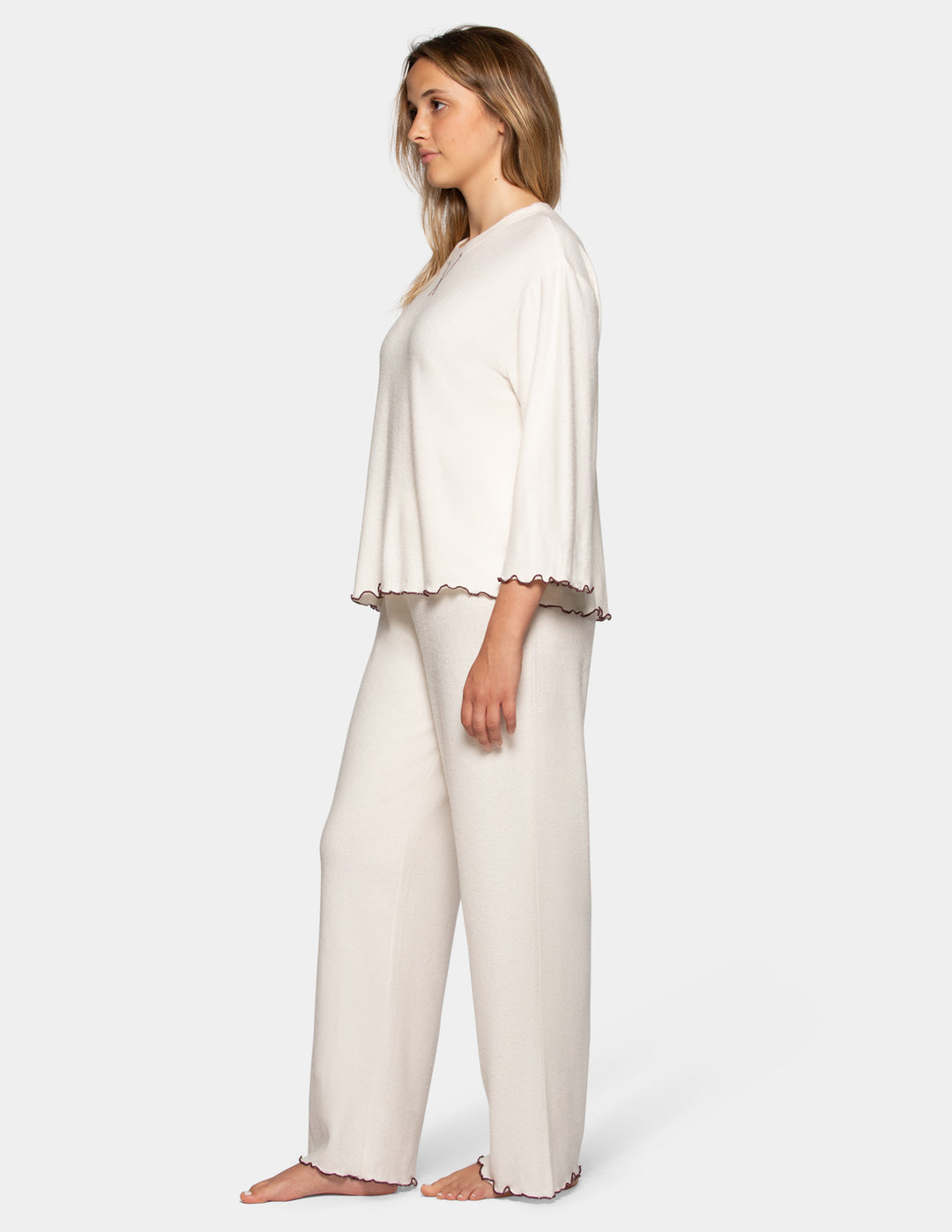 A model wearing an off-white pajama set featuring long pants and a long sleeve matching shirt.