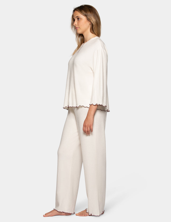 A model wearing an off-white pajama set featuring long pants and a long sleeve matching shirt.