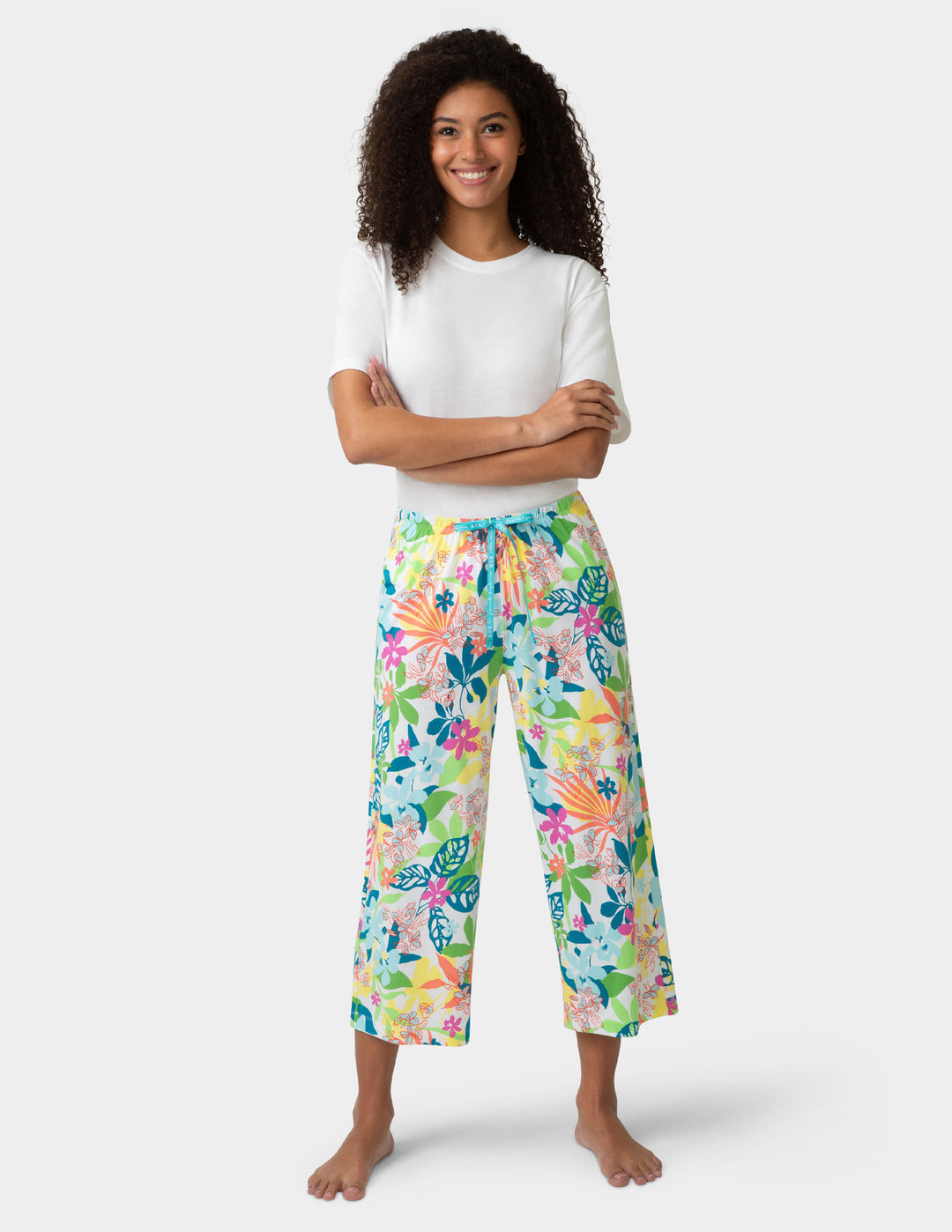 Woman wearing a white top and colorful floral pj pants on a white background