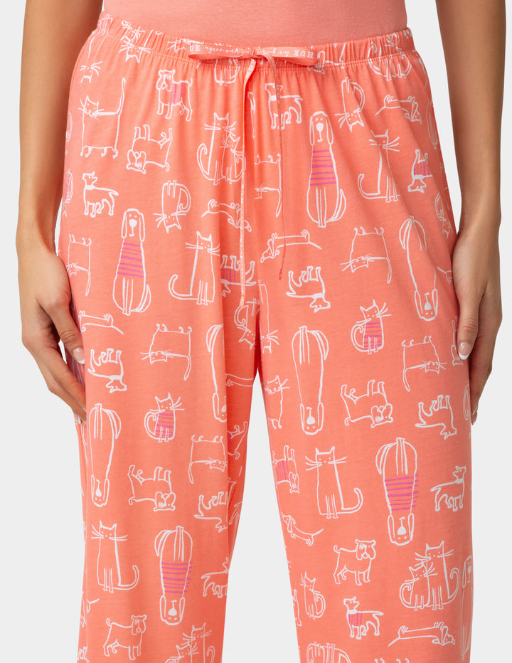 Coral pajama pants with cat pattern worn by a person on a white background