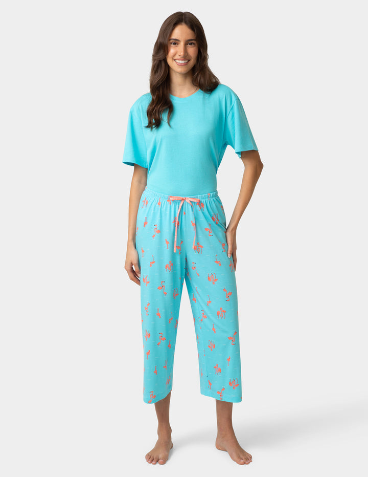 Woman wearing a turquoise pajama set with pink flamingo pattern on a white background
