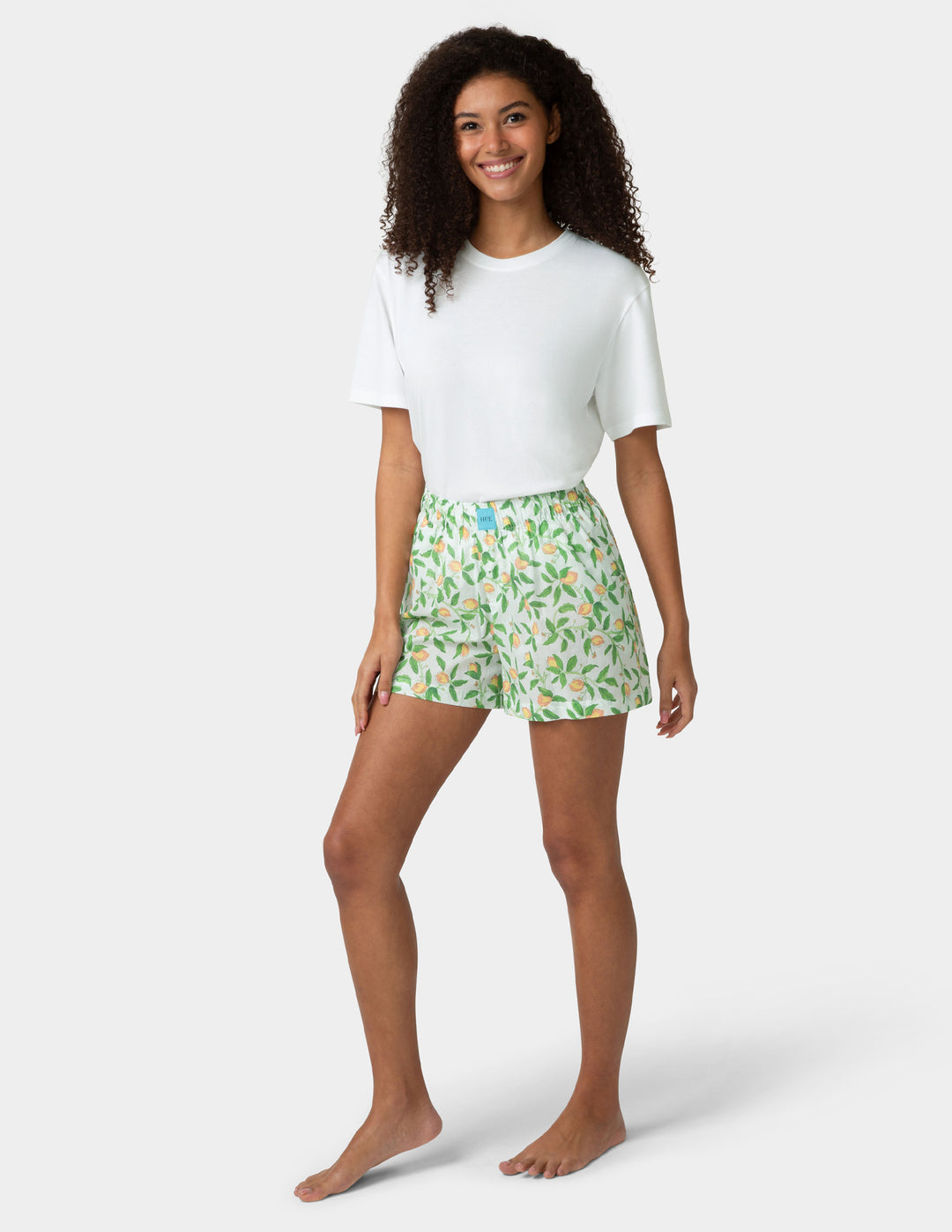 Woman wearing a white t-shirt and green floral pj boxers on a white background