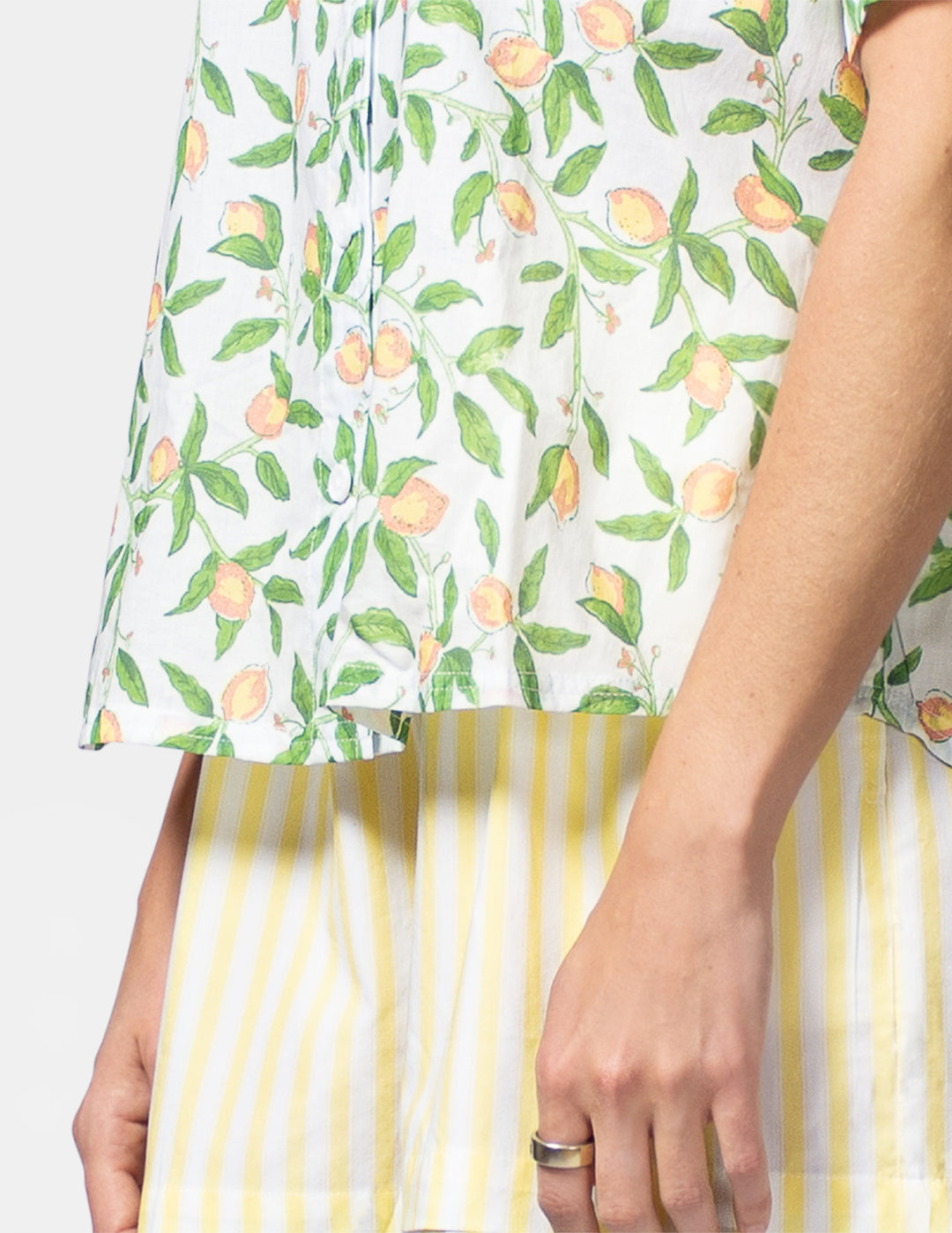 Person wearing a white shirt with lemon and leaf pattern and yellow striped shorts.