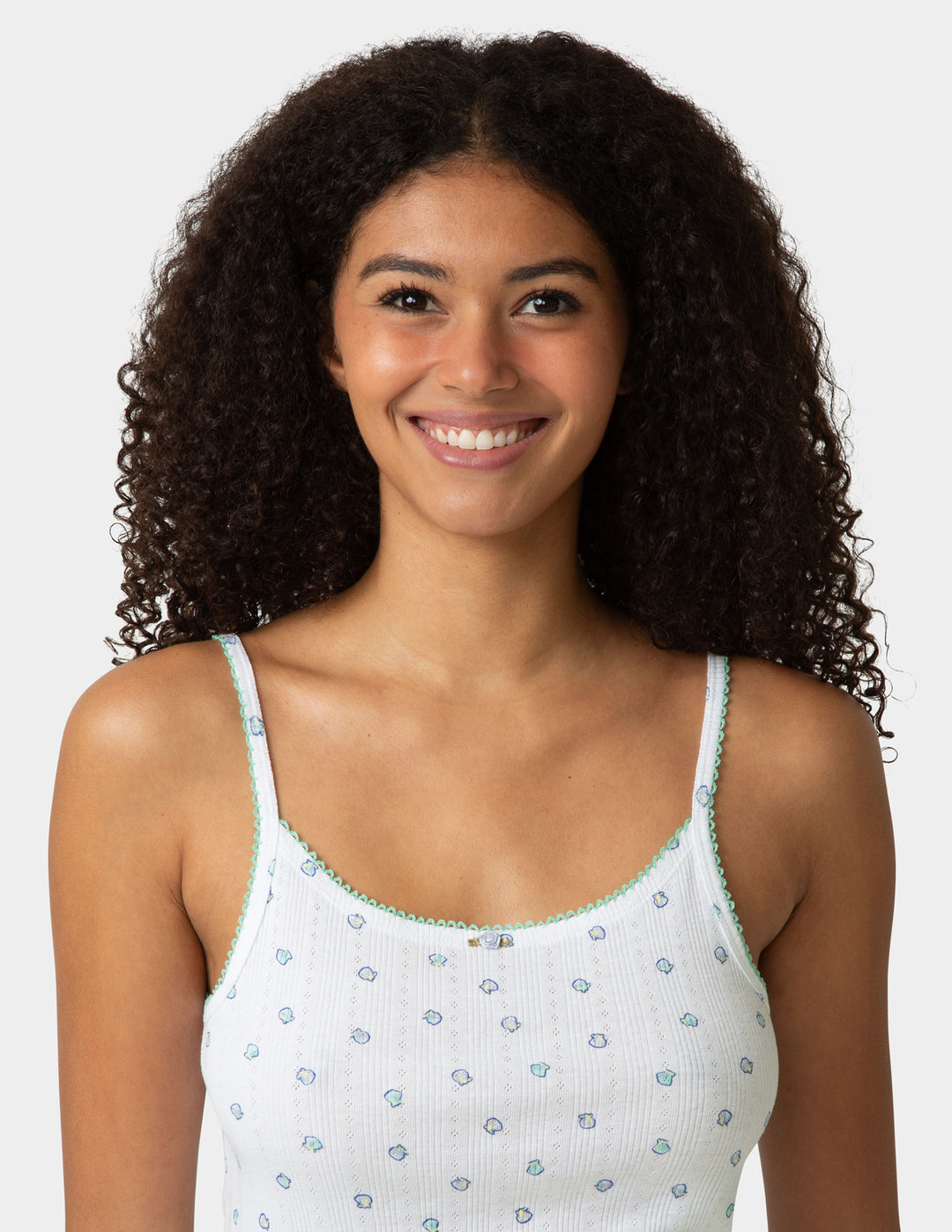 Woman wearing a white camisole with a shell patterns on a plain background