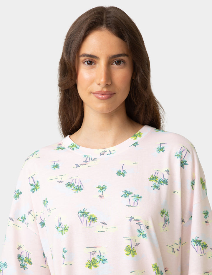 Woman wearing a light pink top with a palm tree pattern on a white background