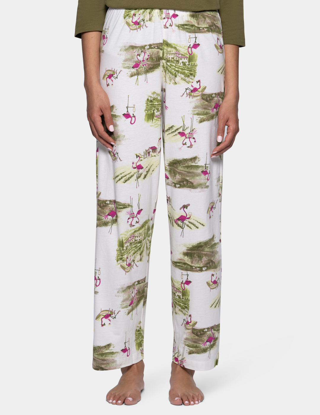 A person wearing white pj pants with an allover print of green palm leaves and pink flamingos, shown from the waist down against a light background.