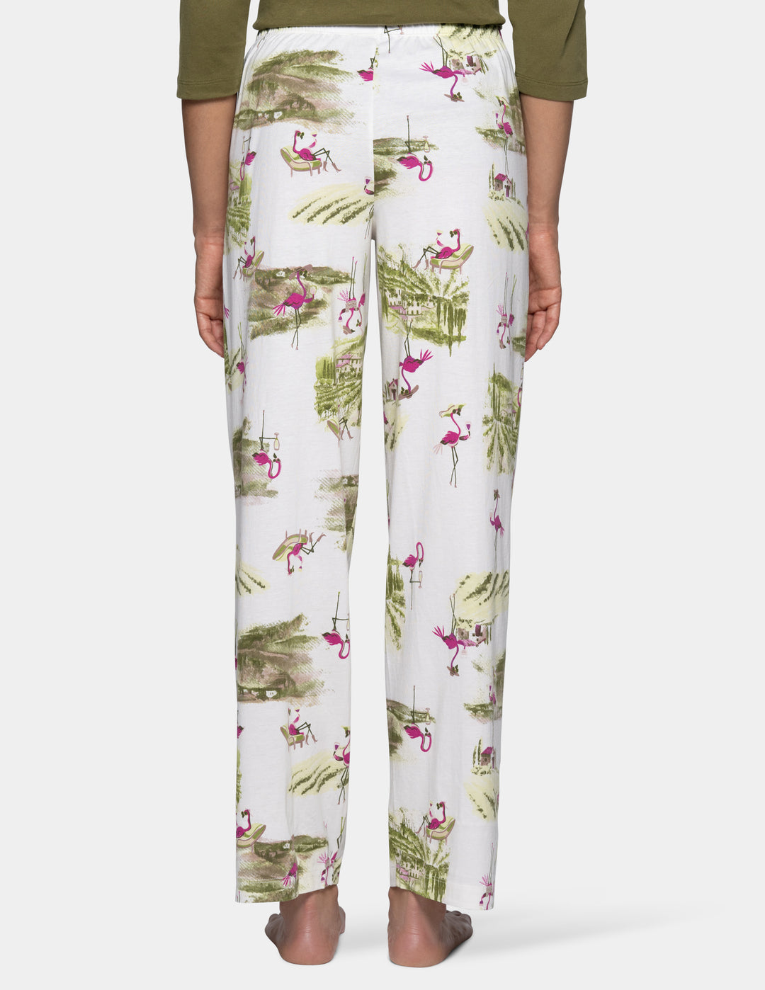 A person wearing white pj pants with an allover print of green palm leaves and pink flamingos, shown from the waist down against a light background.