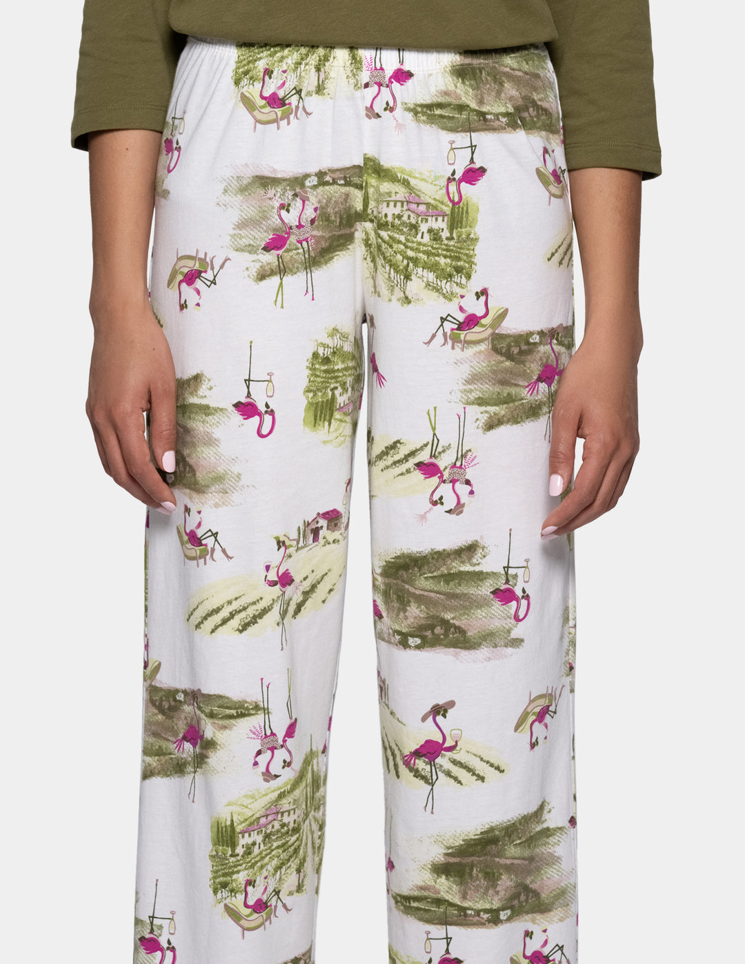 White pajama pants featuring a tropical print of pink flamingos and green palm trees, shown on a model wearing an olive green top.