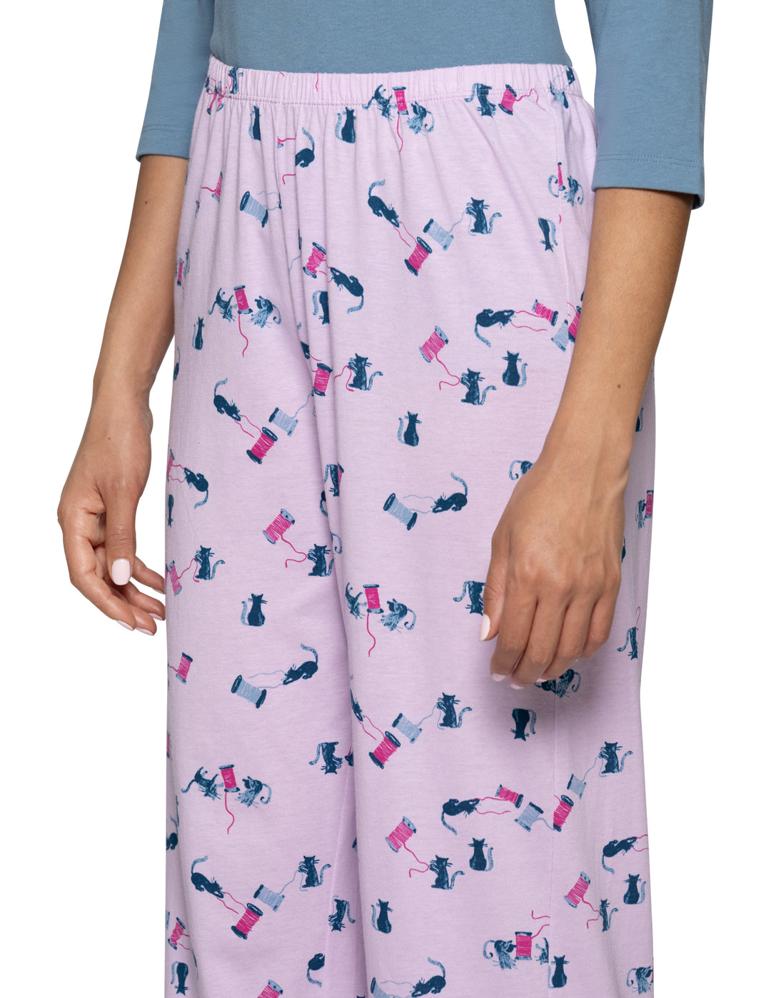 A model is shown from the waist down wearing light purple pajama pants with a cat pattern, paired with a light blue top against a light gray background.