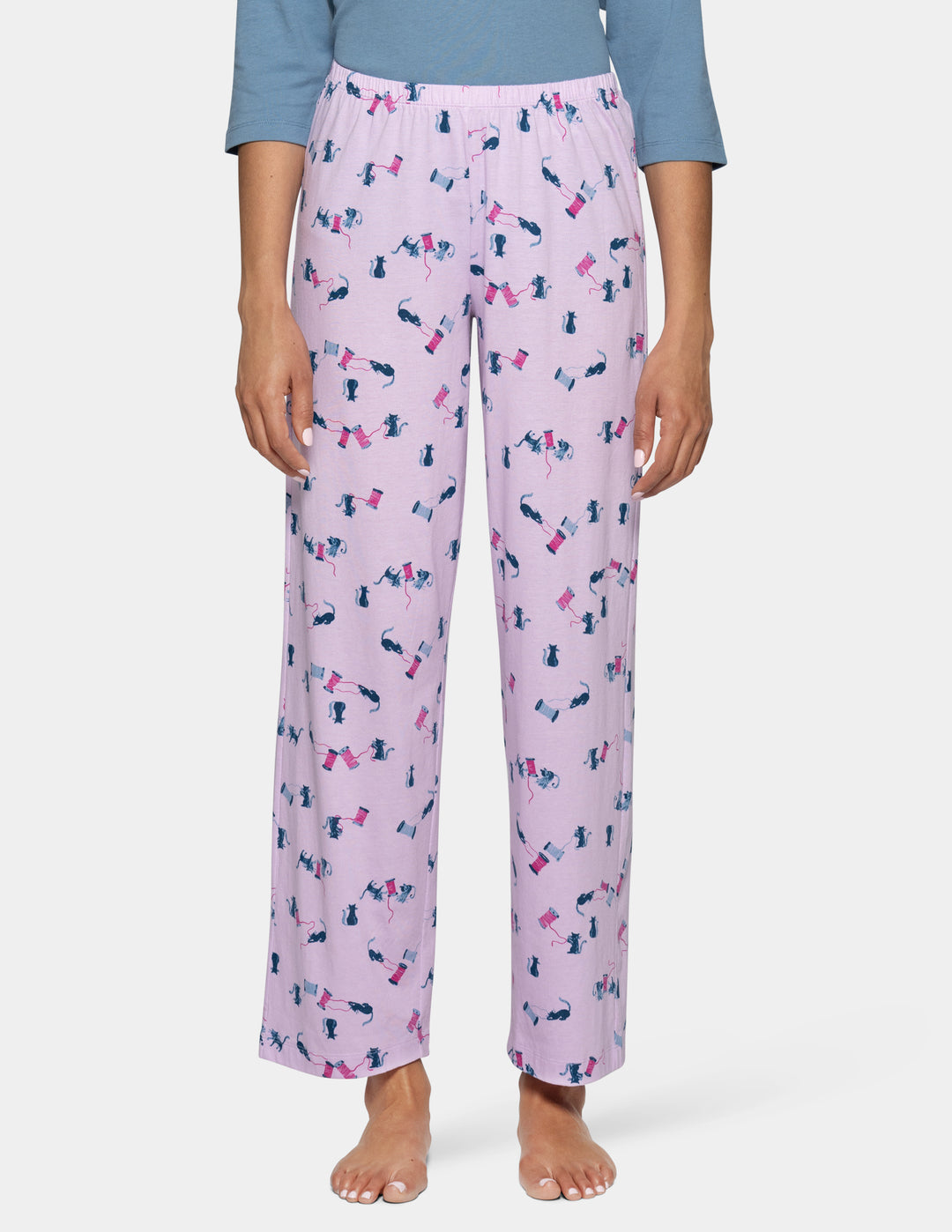 A model is shown from the waist down wearing light purple pajama pants with a cat pattern, paired with a light blue top against a light gray background.