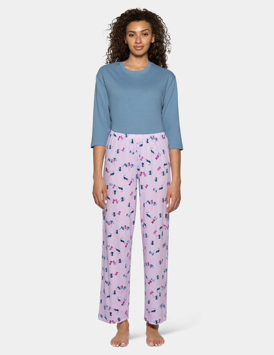 A model wearing light purple pajama pants with a cat pattern, paired with a light blue top against a light gray background.