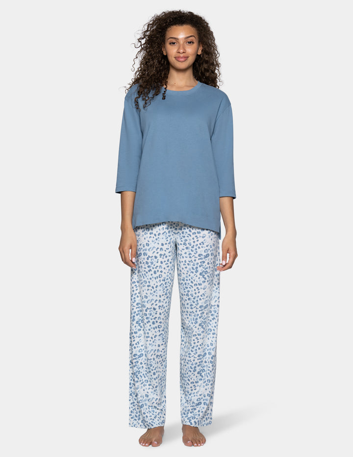 A model wearing high-waisted, wide-leg pajama pants with a blue and white abstract leopard print, paired with a light blue top, shown against a light gray background.