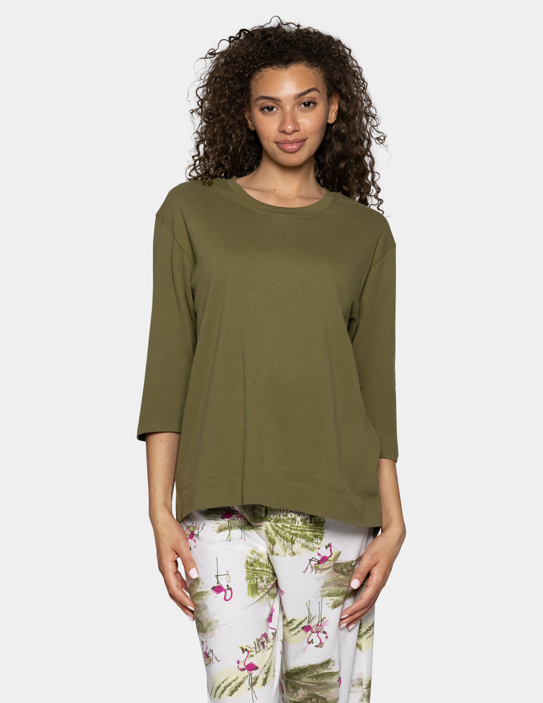 A woman modeling a loose-fitting olive green three-quarter sleeve top paired with white tropical flamingo print pants, set against a solid light gray background.