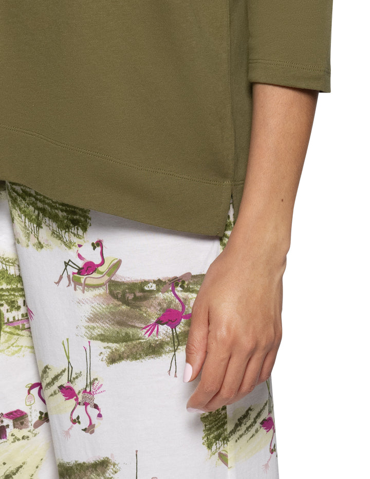 Close-up of a person wearing an olive green short-sleeve top and white printed pants with pink flamingos and green scenery.