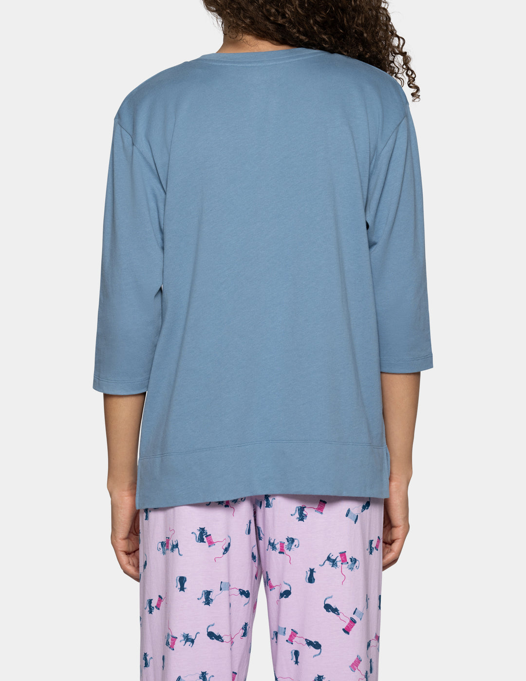 A person shown from the back wearing a light blue three-quarter sleeve top and pink patterned pajama pants against a plain light gray background.
