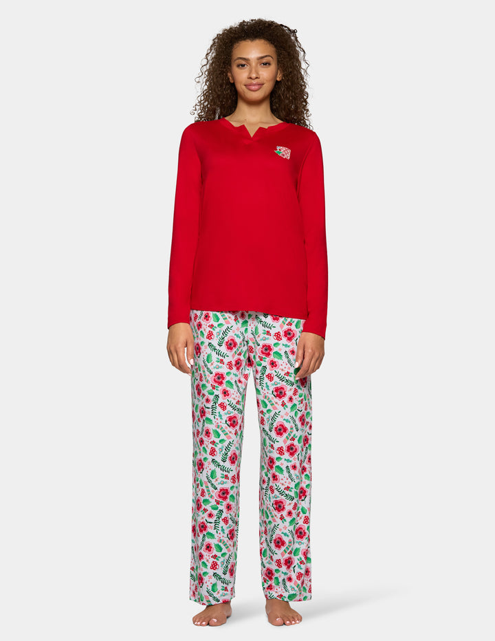 A woman wearing a red long sleeve pajama top with floral full length pajama pants against a gray background.