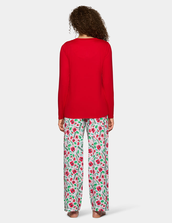 A backside view of a woman wearing a red long sleeve pajama top with floral full length pajama pants against a gray background.