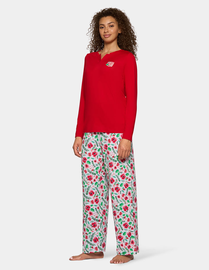 A sideview of a woman wearing a red long sleeve pajama top with floral full length pajama pants against a gray background.