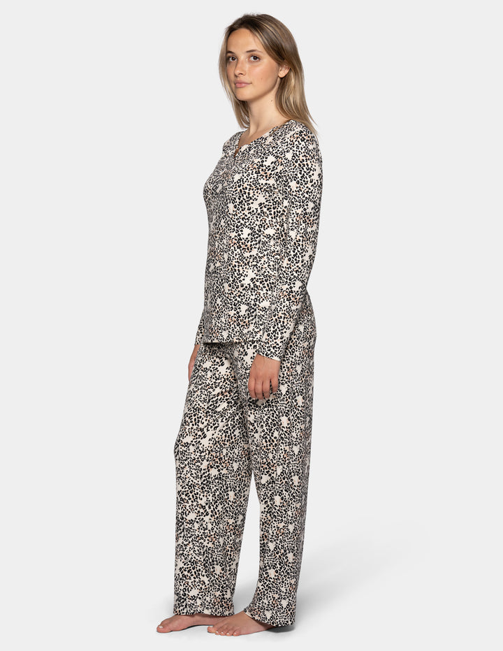 A sideview of a model wearing a matching pajama set featuring a long sleeve top and full length pants with an animal print pattern.