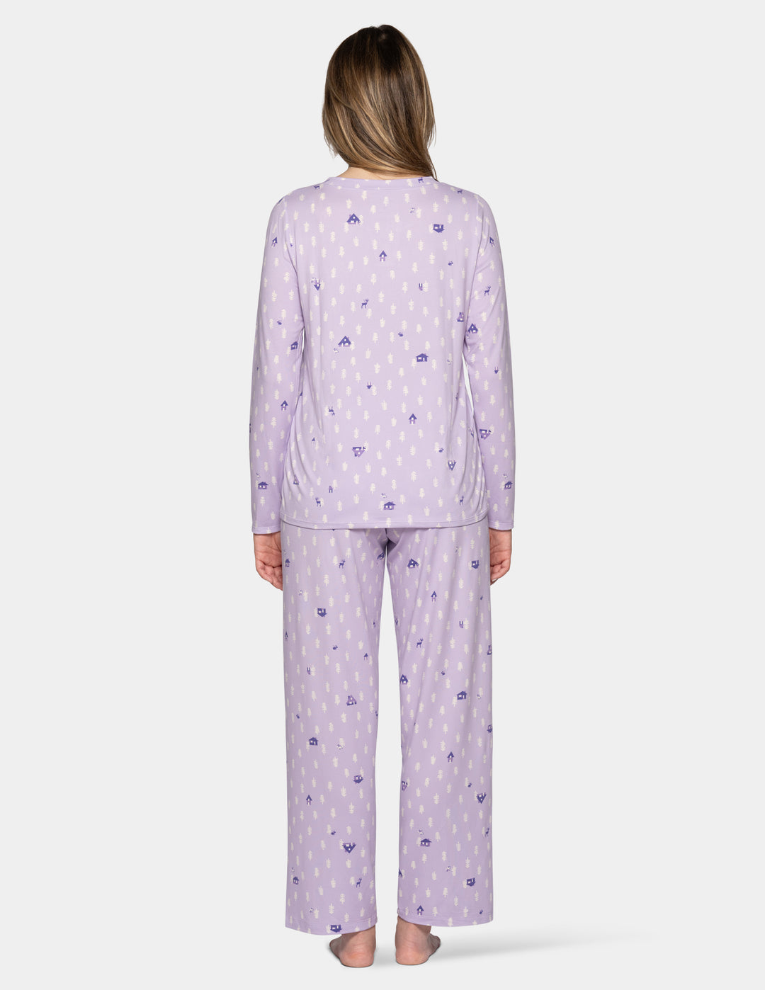 A woman viewed from the back wearing a light lavender pajama set with a small repeating purple and white pattern, standing against a plain light gray studio background.