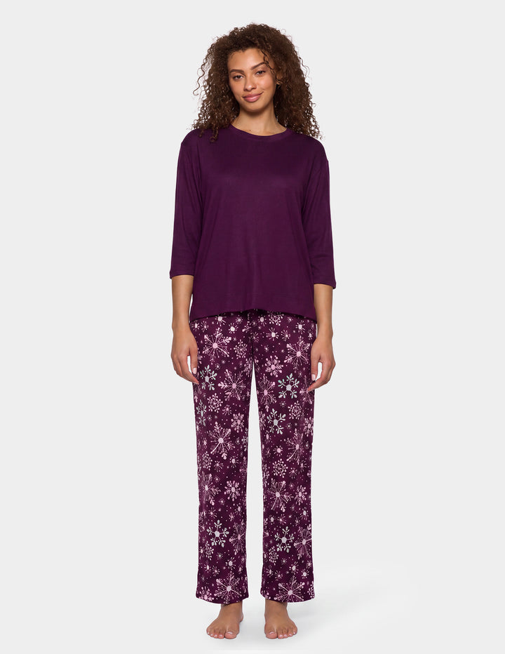 A model wearing a purple pajama top and matching purple snowflake pajama pants.