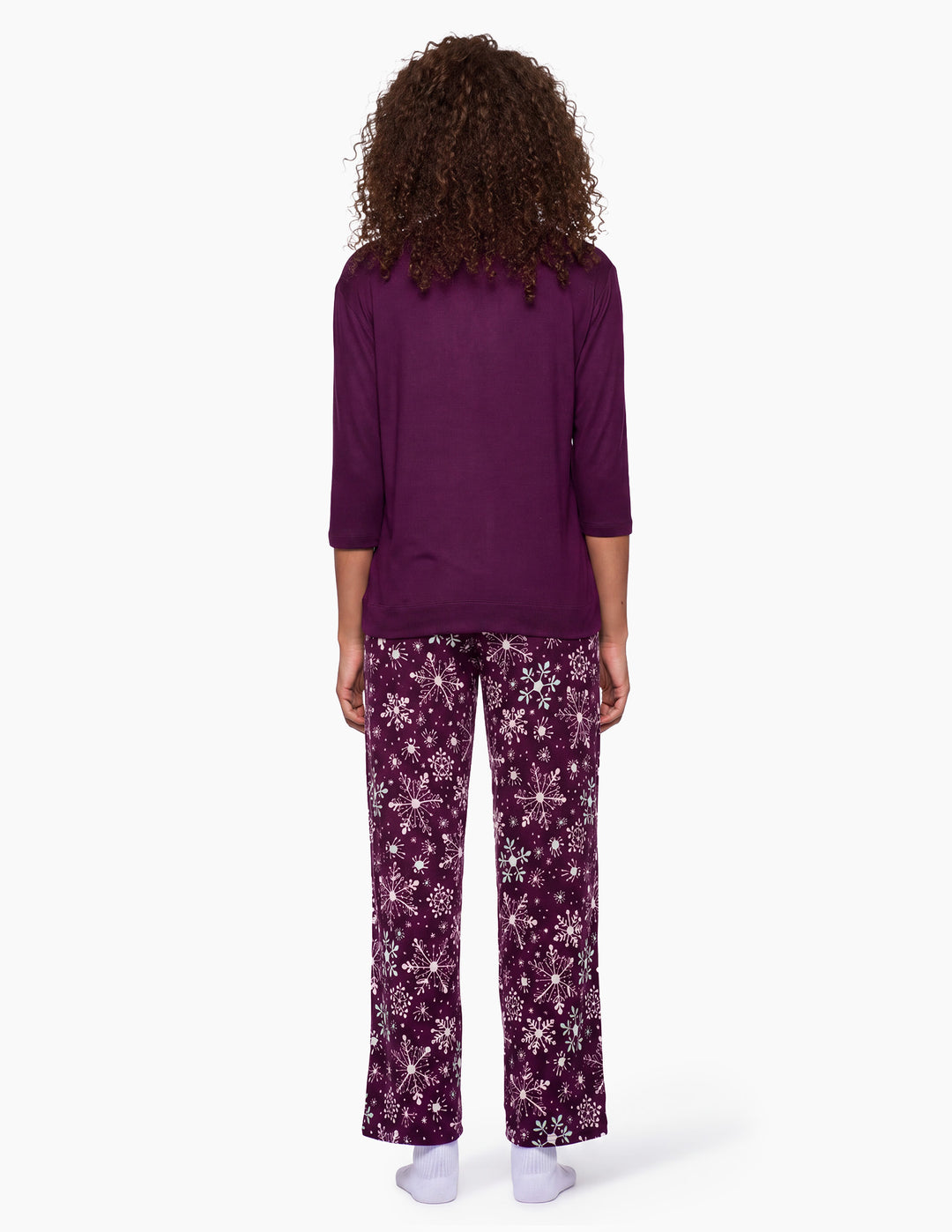 A backside view of a model wearing a purple pajama top and matching purple snowflake pajama pants.